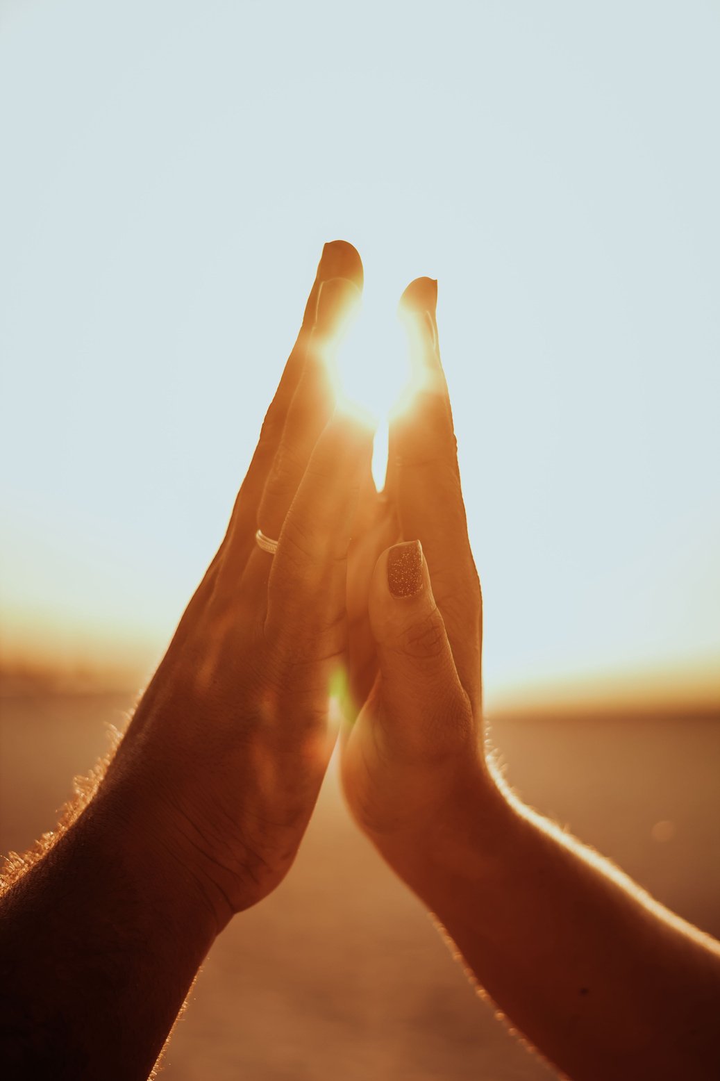 Crop unrecognizable loving couple touching hands against bright sunset